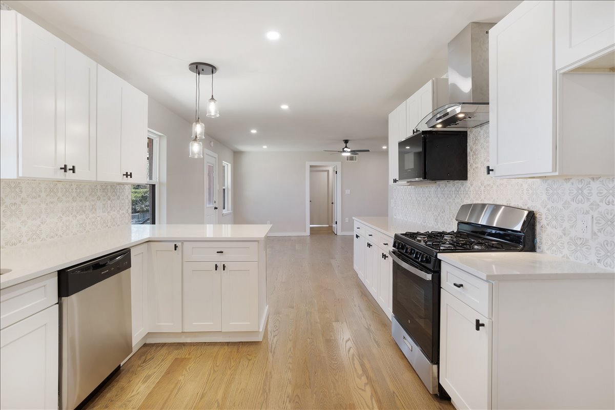 Renovated white kitchen with gas range, pendant lights and hardwood floors